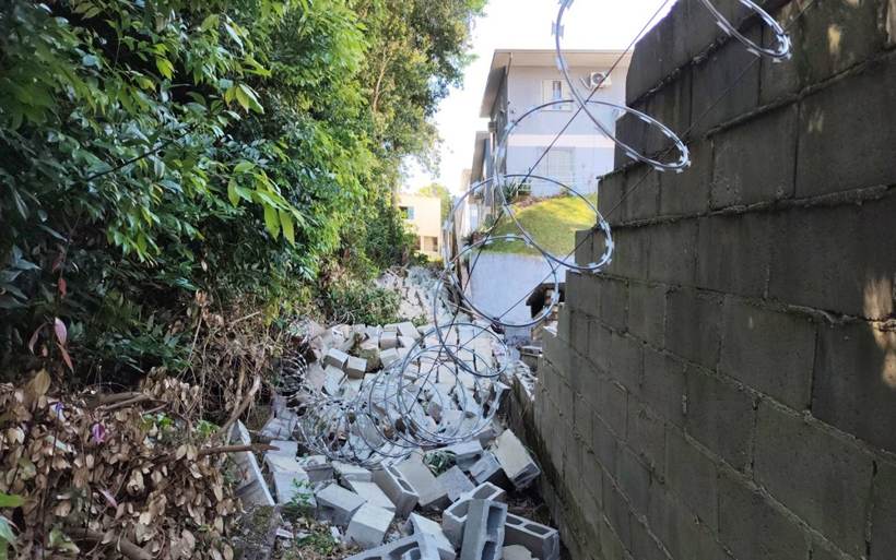Trecho colapsado do muro de divisa, com blocos de concreto e concertina caídos no terreno vizinho