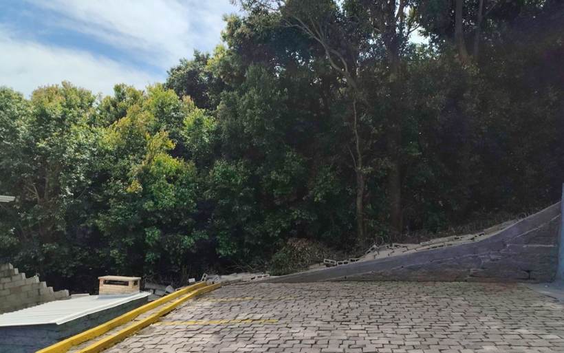 Visão geral do trecho colapsado do muro de divisa, com blocos caídos ao longo da contenção junto ao estacionamento